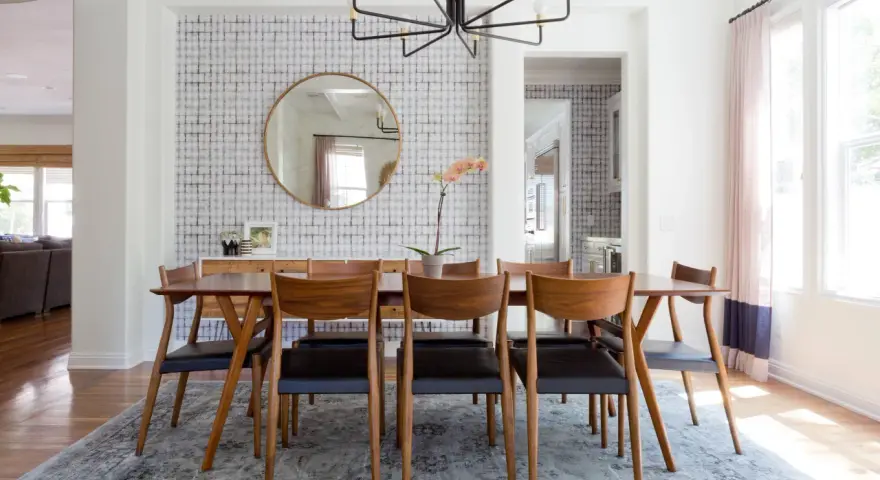 Tavolo da pranzo in legno con sedie in pelle nera, tappeto sotto il tavolo da pranzo si, con carta da parati a motivi geometrici e specchio rotondo.