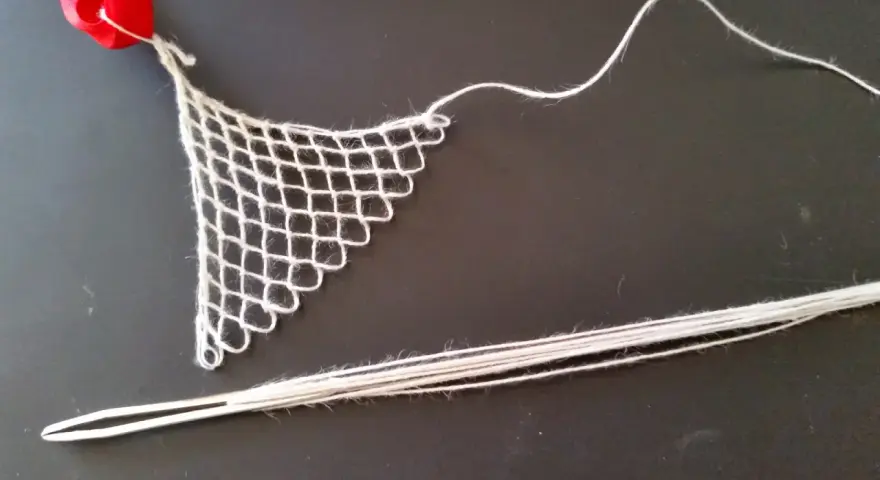 Un ago con filo bianco e un pezzo di rete a maglie, un tipo di ricamo eseguito su una rete a maglie, con un nastro rosso in alto.