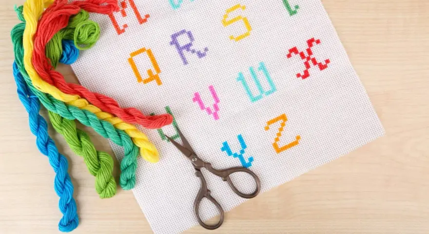 Fili colorati e forbicine pronti per ricamare nomi punto catenella su tela bianca con lettere dell'alfabeto.
