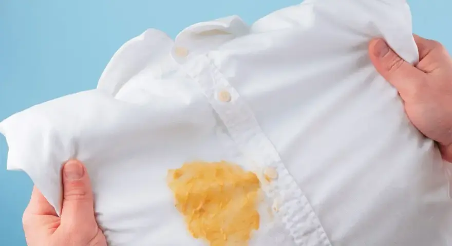 Come togliere le macchie gialle dalla biancheria colorata: una camicia bianca macchiata di giallo, tenuta in mano.