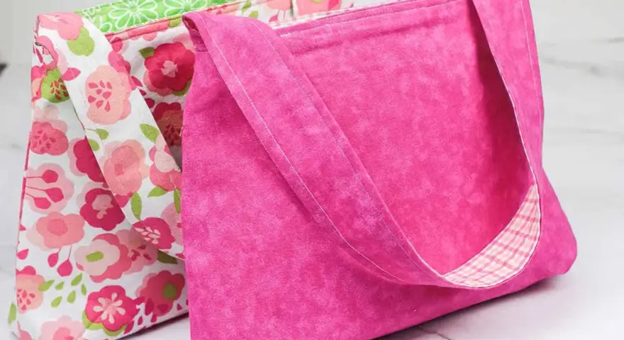 Two handmade fabric bags, one pink with a floral pattern, the other solid pink with a plaid lining.