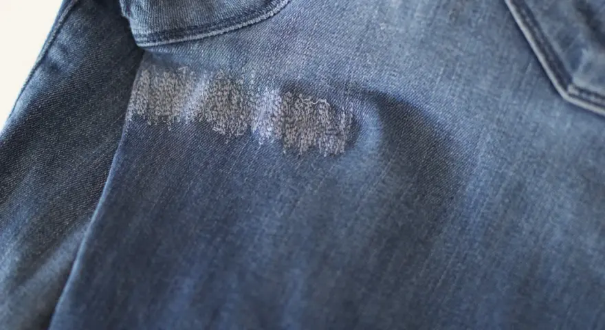 Dettaglio di un tessuto di jeans blu con un'area rattoppata con filo bianco, che mostra la cura nel rattoppare jeans.