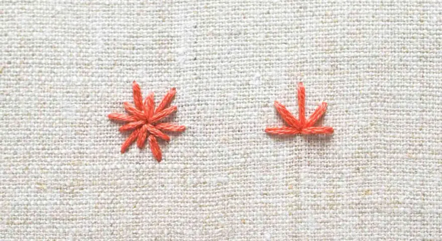 Two orange embroidery stitches on a textured linen fabric.