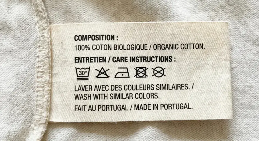 Etichetta con simboli tessuti: lavaggio 30°, non candeggiare, stirare a bassa temperatura, non lavare a secco, non asciugare in asciugatrice. 100% cotone biologico, fatto in Portogallo.