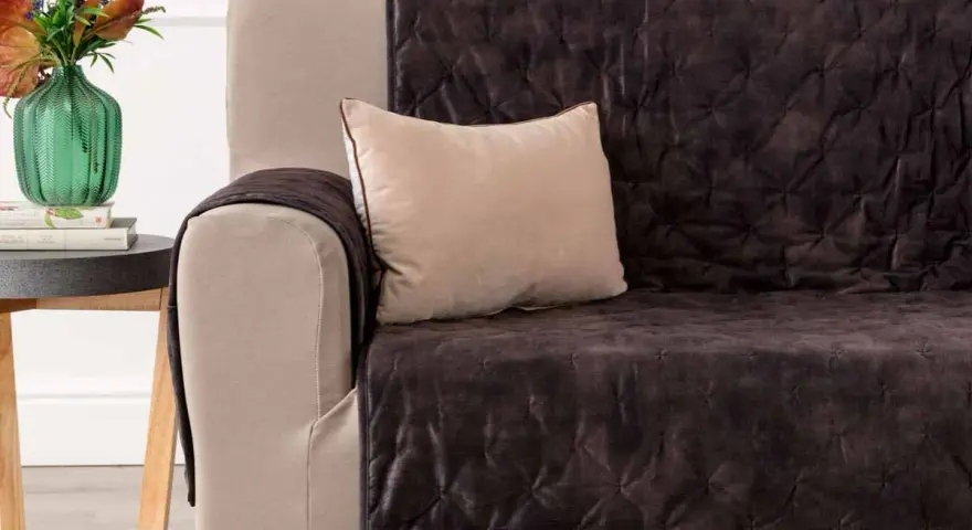 Divano con copridivano trapuntato marrone scuro, un cuscino beige e un vaso di fiori. Il miglior tessuto per divani per un look accogliente.
