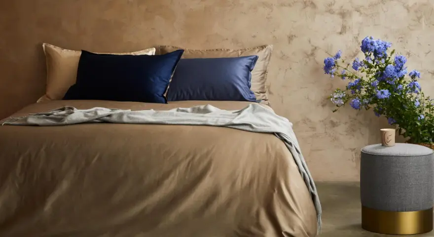 Letto con lenzuola color tabacco, cuscini blu e beige, coperta grigia. Il miglior tessuto per lenzuola per un sonno di qualità.