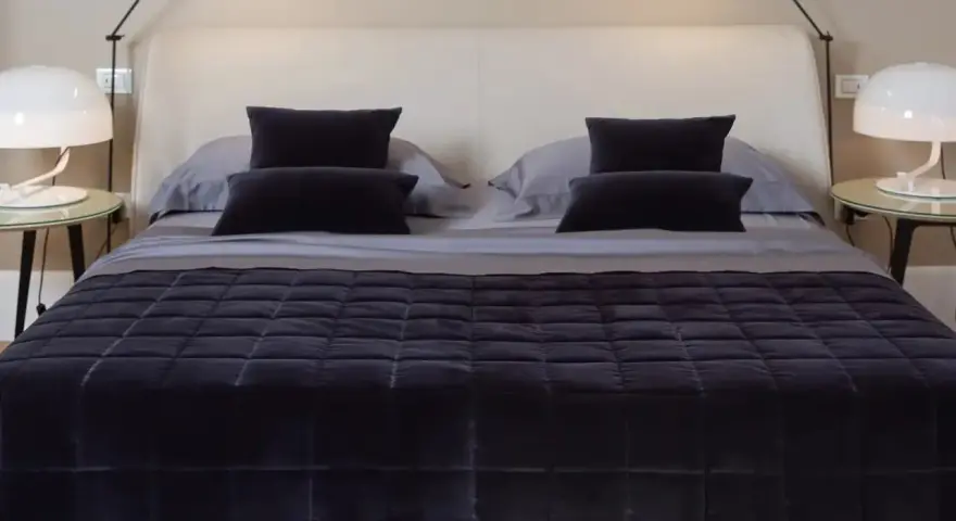 Un letto impeccabile, con copriletto trapuntato scuro e cuscini coordinati, mostra come rifare il letto in modo elegante.