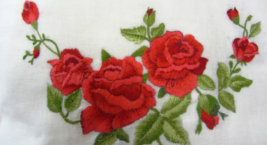 Ricamo di rose rosse su tessuto bianco, un delicato punto pittura che evoca un giardino fiorito.