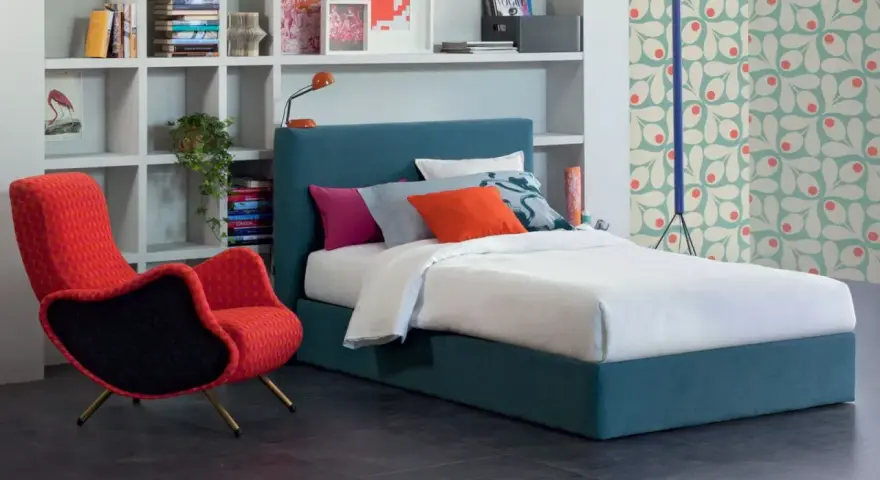 Letto una piazza e mezza con testiera blu, cuscini colorati e una poltrona rossa vivace.
