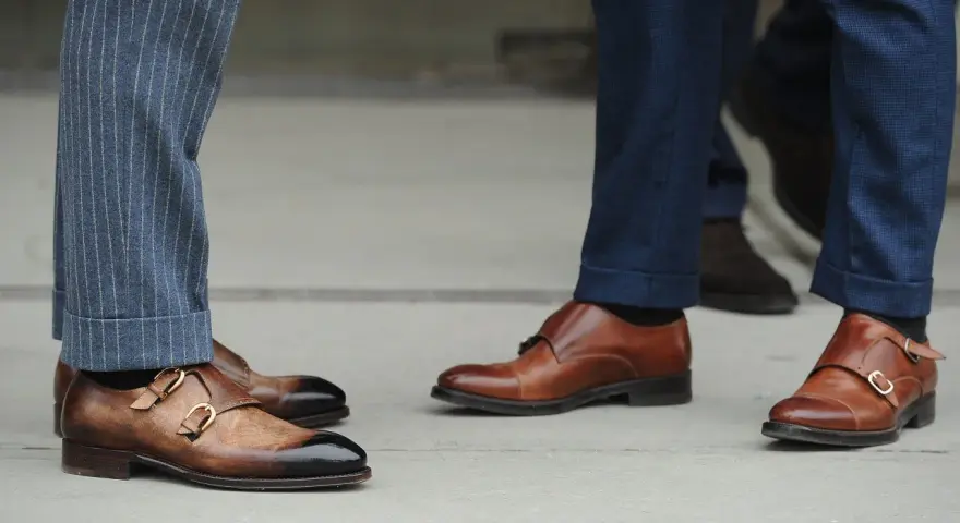 Primo piano su scarpe monk strap marroni e diversi tipi di orlo pantaloni: a risvolto e con pinces.