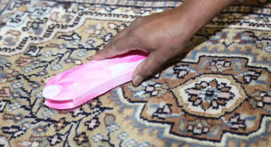 Mano che pulisce un tappeto persiano con una spazzola rosa. Sorprendentemente, si possono lavare i tappeti persiani in lavatrice con cura.