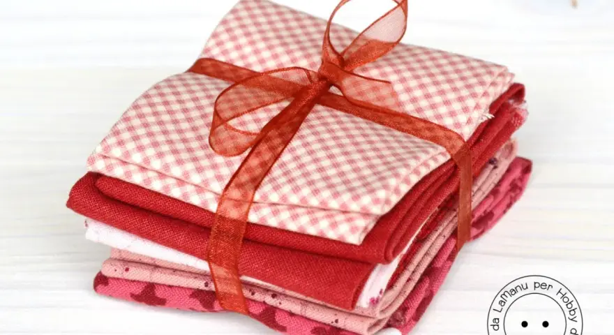 Fazzoletti di stoffa rossi e rosa, con fantasie a quadretti e cuoricini, legati da un nastro. Perfetti per un progetto di cucito creativo.