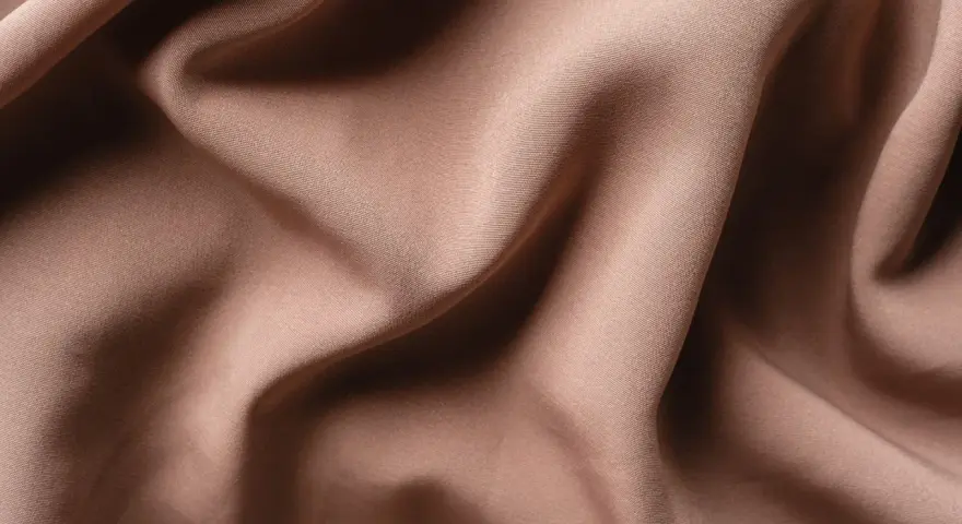 Tessuto di raso color tortora, morbido e drappeggiato, che mostra la sua texture fine. Il raso si può stirare per ottenere una finitura impeccabile.