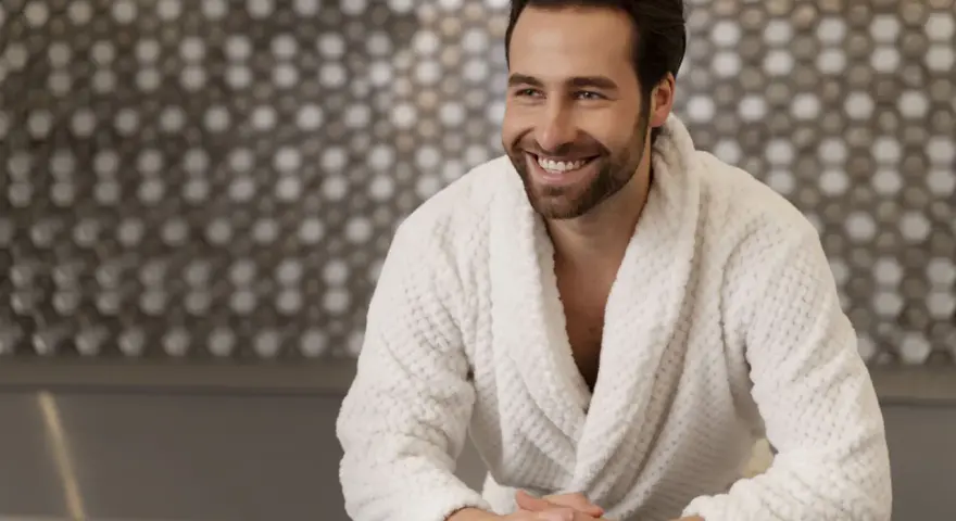 Uomo sorridente in un morbido accappatoio che asciuga bene, con uno sfondo a mosaico.