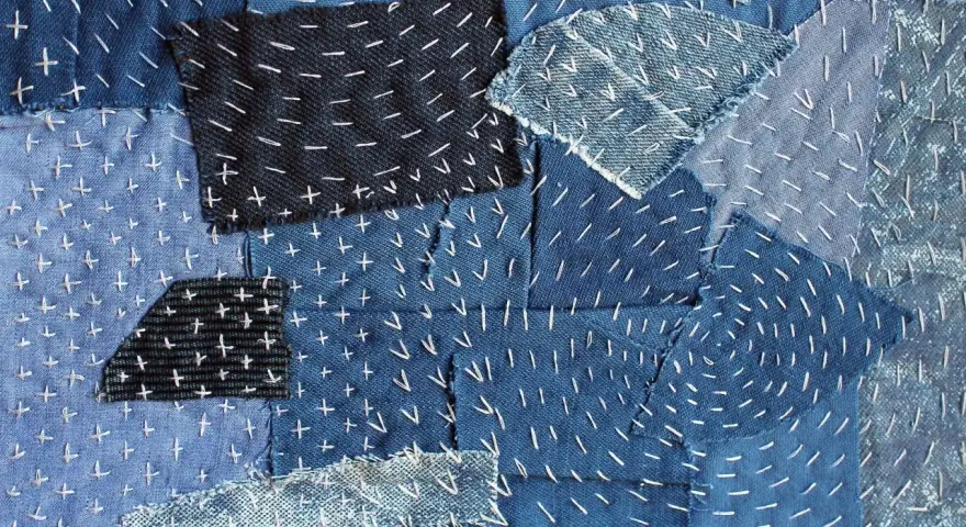 Tessuto patchwork in denim con cuciture bianche a punto croce e a zig-zag, un esempio di rammendo giapponese.