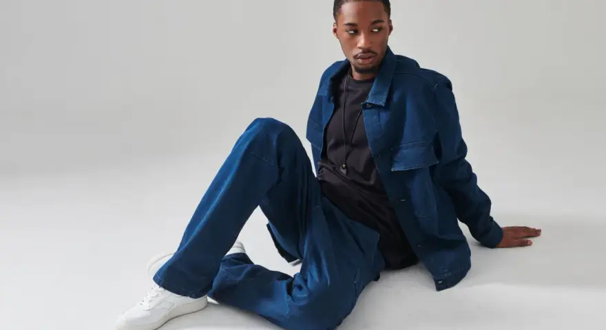 Un uomo con un completo di jeans blu, seduto a terra. Chissà quanto pesa un paio di jeans così comodi.