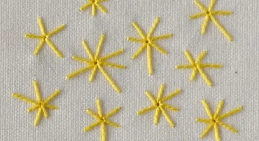 Piccole stelle gialle ricamate a punto pieno su tessuto bianco. Un esempio di come ricamare una stella a punto pieno.