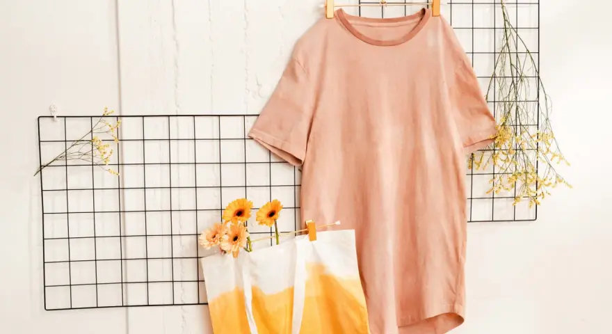 T-shirt rosa e borsa con sfumature arancioni, ispirazione per come tingere un vestito. Fiori e rametti secchi decorano.