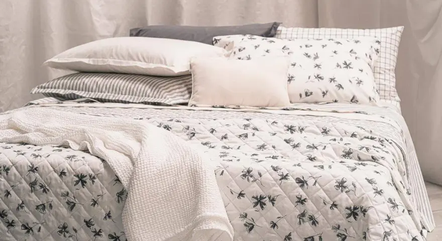 Un letto accogliente con biancheria a fiori e righe, coperte morbide e cuscini che invitano al riposo, come in un sogno di letti all'americana.