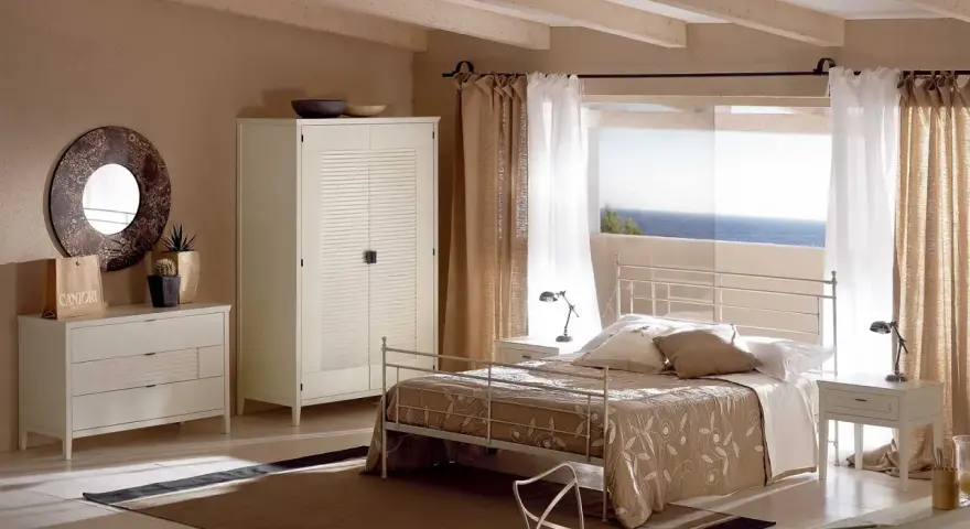 Camera da letto con letto tortora, armadio bianco e cassettiera. Abbinamenti eleganti per un ambiente rilassante con vista mare.