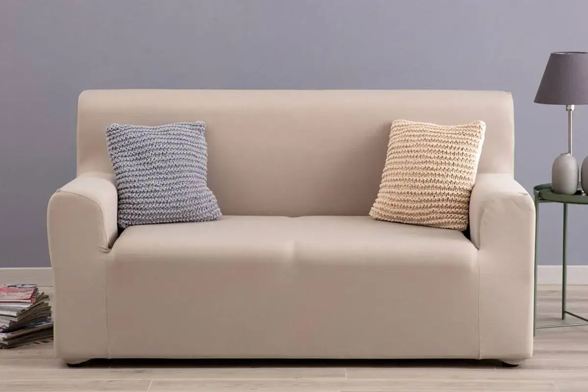 Divano beige con due cuscini decorativi. Scopri come lavare copridivano in lavatrice per mantenerli sempre freschi e puliti.