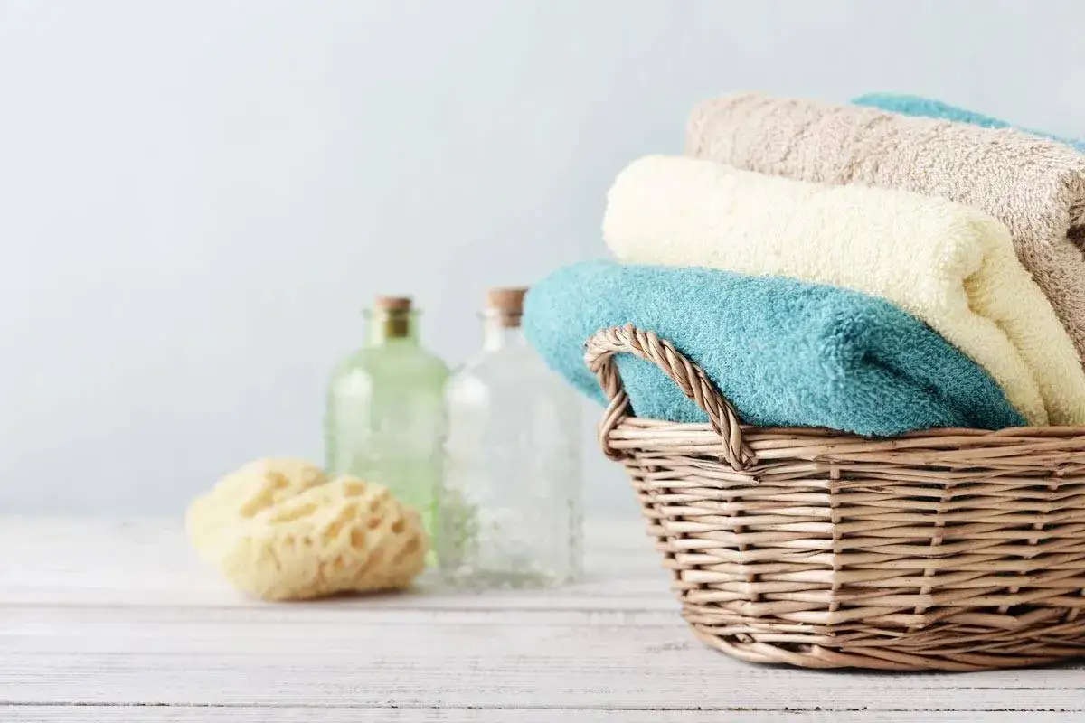 Cesto di vimini con asciugamani morbidi, rimedi della nonna per un bagno rilassante. Accanto, spugna naturale e bottiglie di vetro.