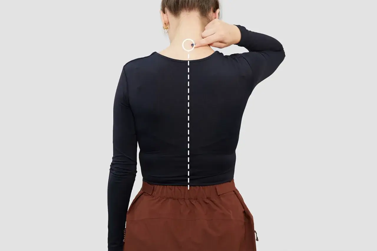 Donna indica un punto sul collo, con una linea tratteggiata che scende lungo la schiena, utile per capire come misurare le spalle donna.