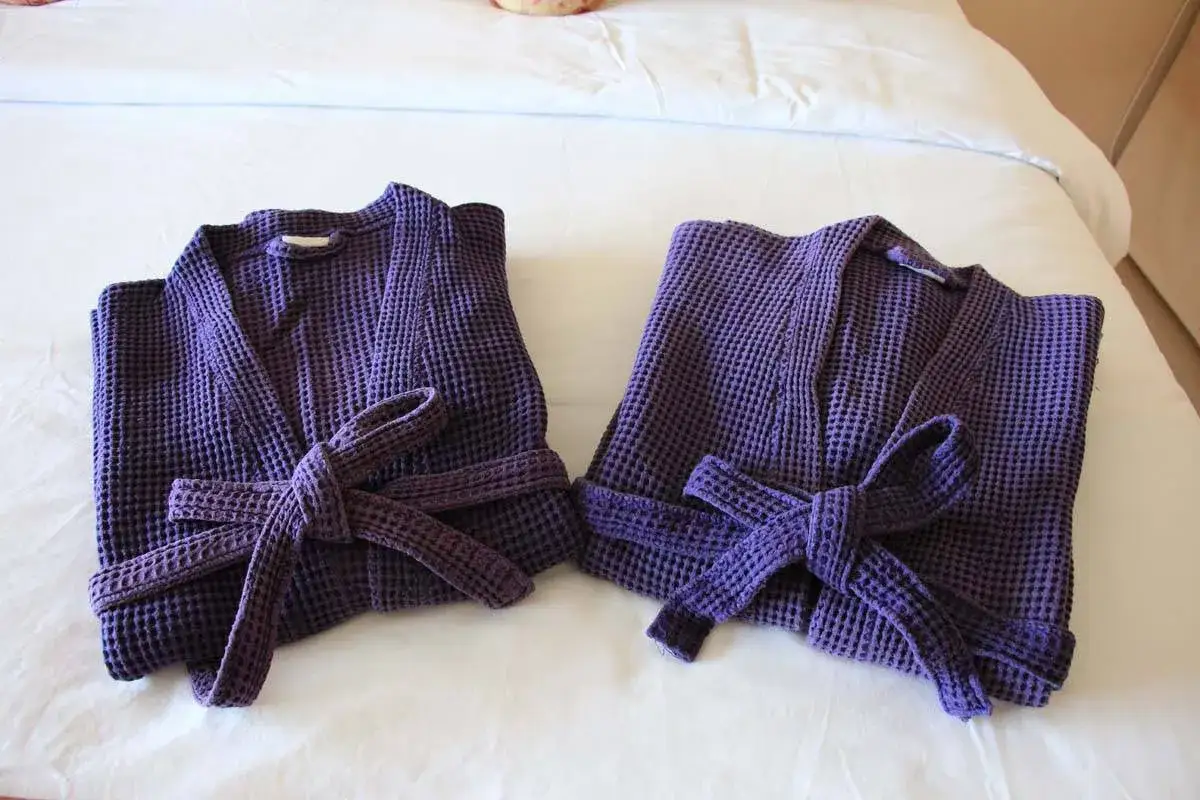 Due accappatoi viola, piegati e legati con il loro stesso tessuto, pronti per essere riposti. Ecco come piegare un accappatoio per un ordine perfetto.