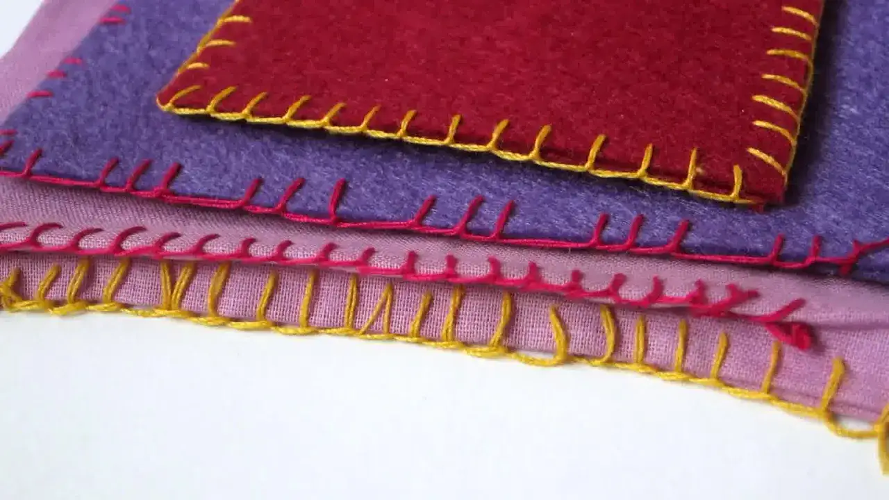 Tessuti sovrapposti con cuciture colorate. Un pezzo rosso bordato di giallo, sotto un viola con filo rosa, e infine un rosa con filo giallo. Un punto coperta che unisce i colori.