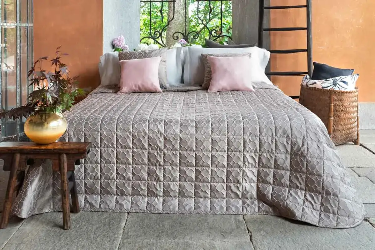 Un letto con copriletto trapuntato, cuscini rosa e un vaso dorato. Ideale per lavare copriletto in lavatrice.
