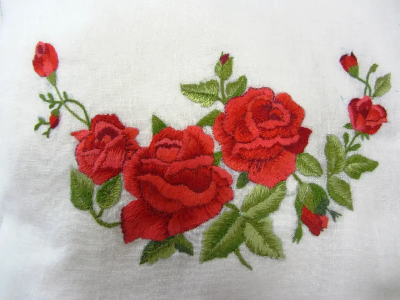 Ricamo di rose rosse su tessuto bianco, un punto pittura che evoca un giardino fiorito.