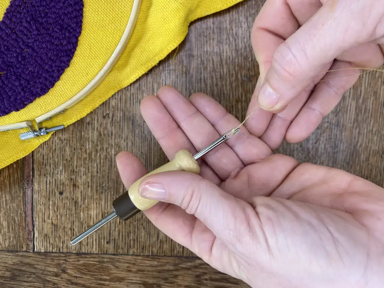 Mani che preparano un filo dorato per un ricamo a mano su tela gialla con un motivo viola.