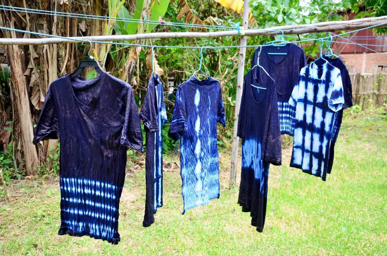 Abiti con motivi tie-dye blu e bianchi appesi ad asciugare, risultato di un esperimento di tingere tessuti sintetici.