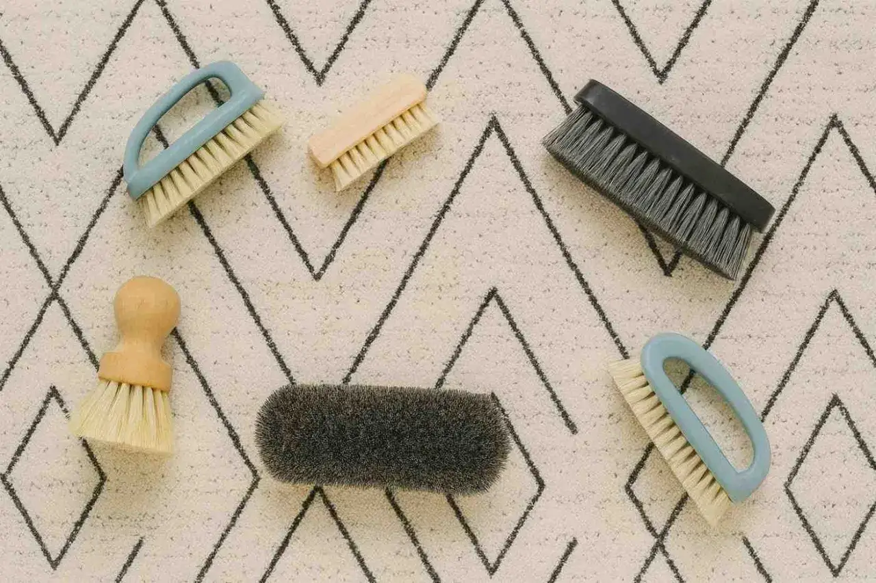 Spazzole di varie forme e dimensioni su un tappeto con motivo a zig-zag, pronte per aiutarti a capire come lavare un tappeto di lana grande.