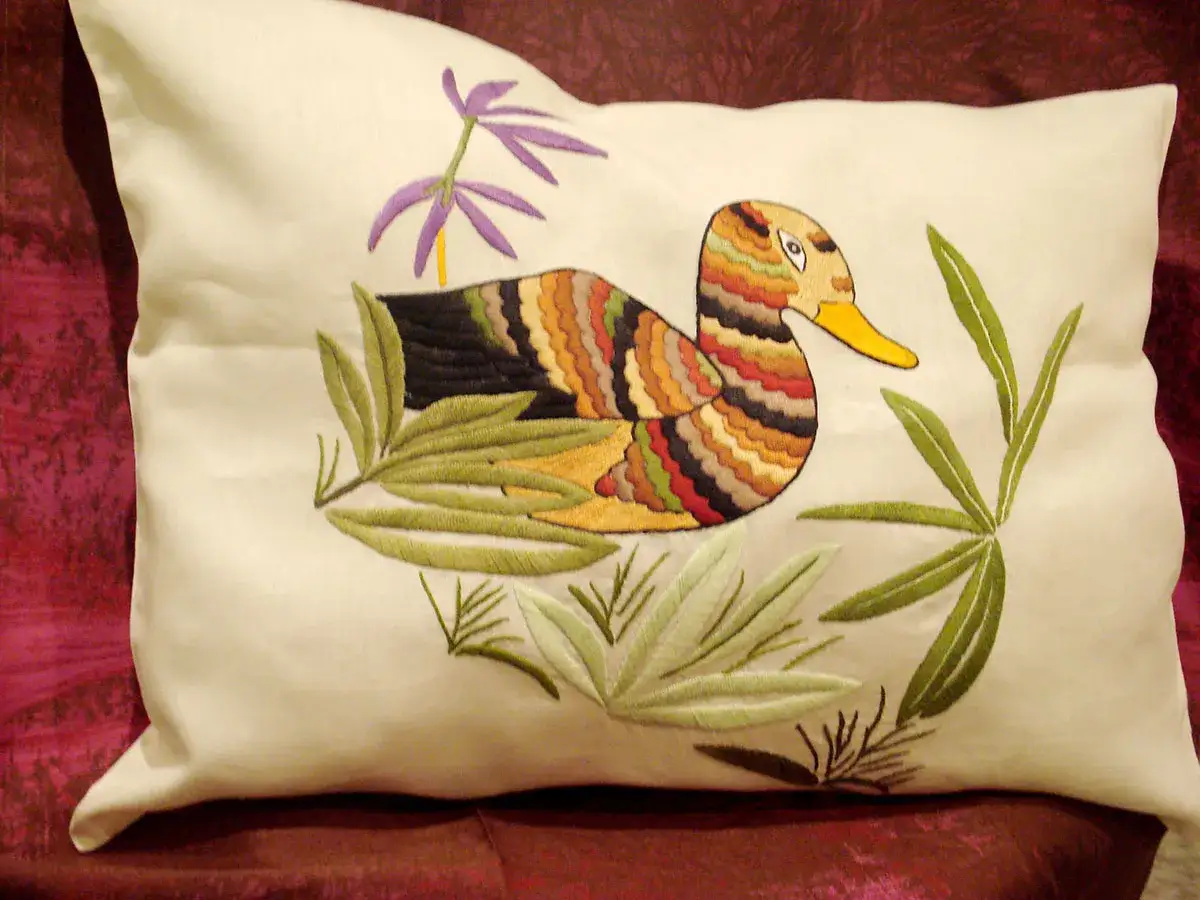 Cuscino con ricamo di un'anatra colorata e piante verdi. Un esempio di rammendi creativi che portano vita e colore.