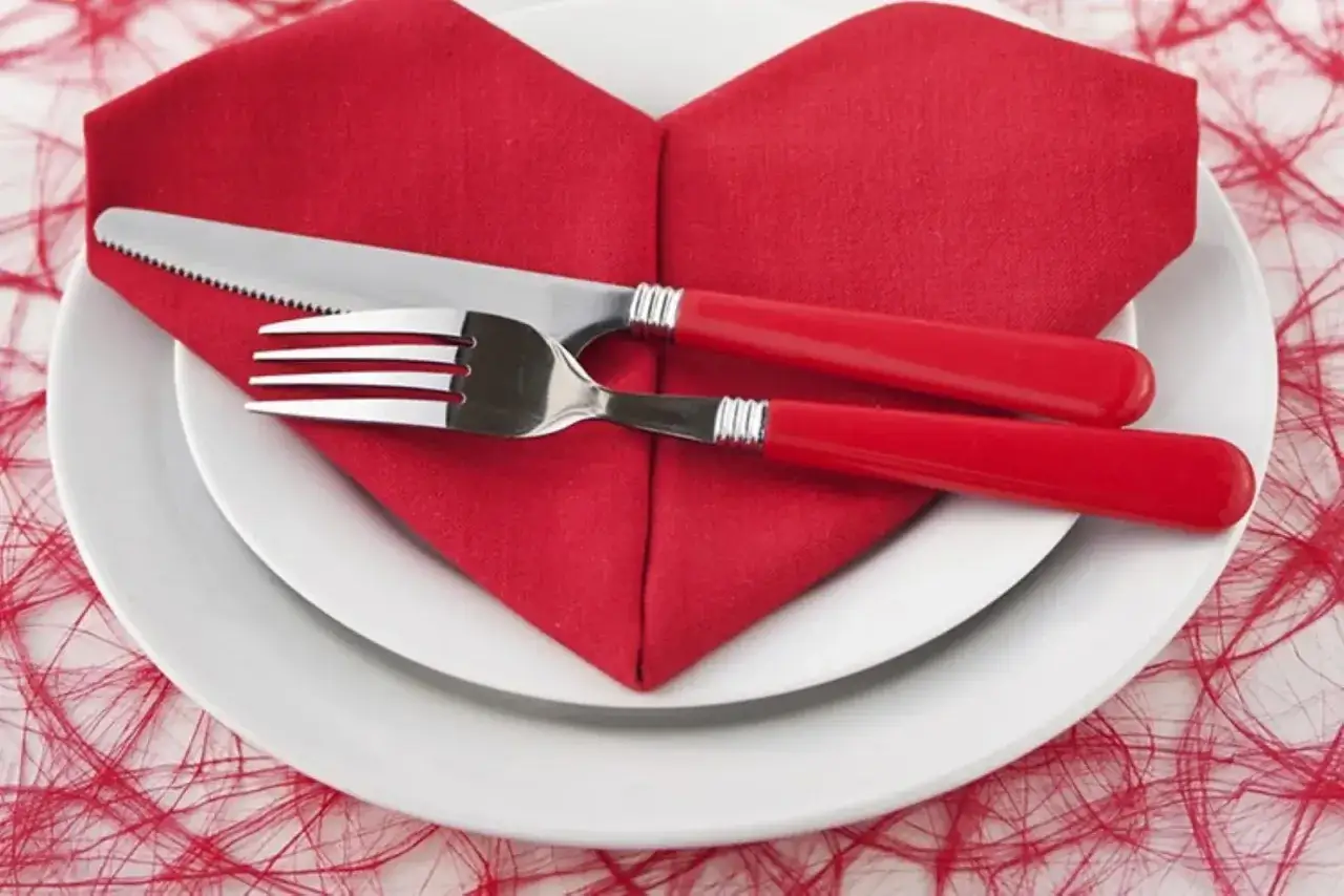 Un tovagliolo rosso a forma di cuore, pronto per un tutorial. Posata rossa e bianca su un piatto bianco.