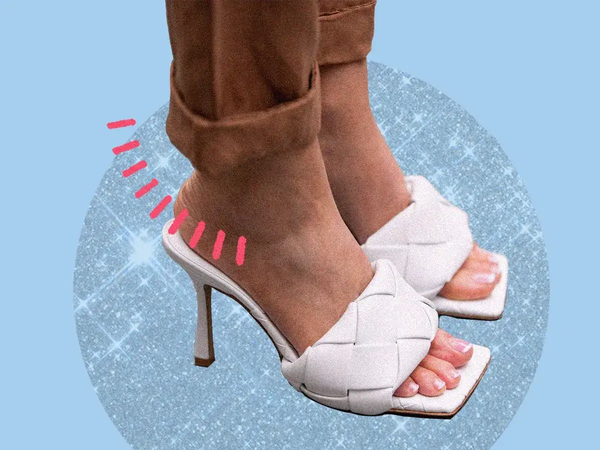 Piedi con sandali bianchi intrecciati e pantaloni marroni con orlo arrotolato. Diversi tipi di orlo pantaloni si abbinano a scarpe eleganti.