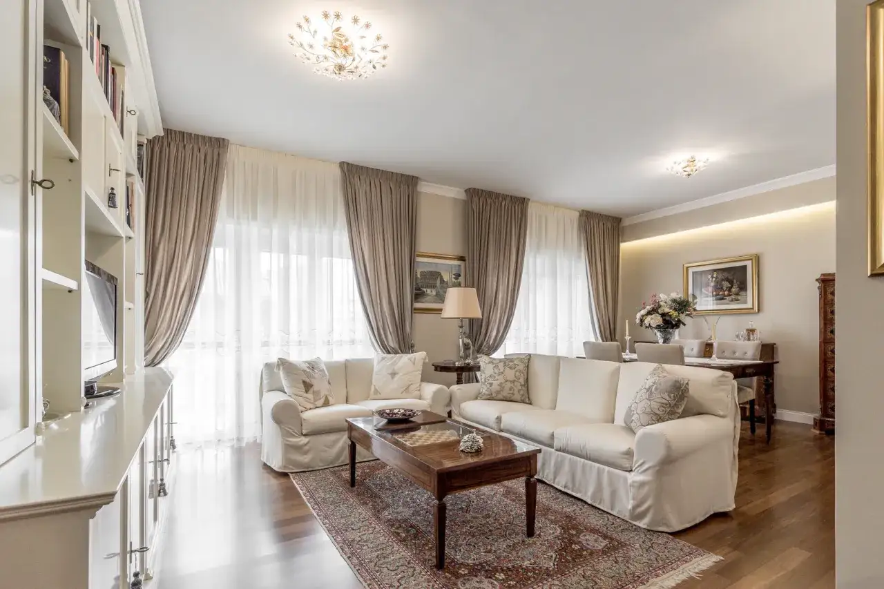 Tende color tortora e bianche nel soggiorno, con divani bianchi e tappeto decorato.