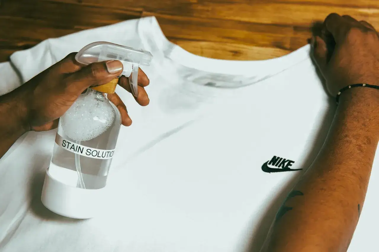 Mano che spruzza una soluzione su una maglia bianca Nike per rimuovere una macchia. Ecco come smacchiare maglia bianca.