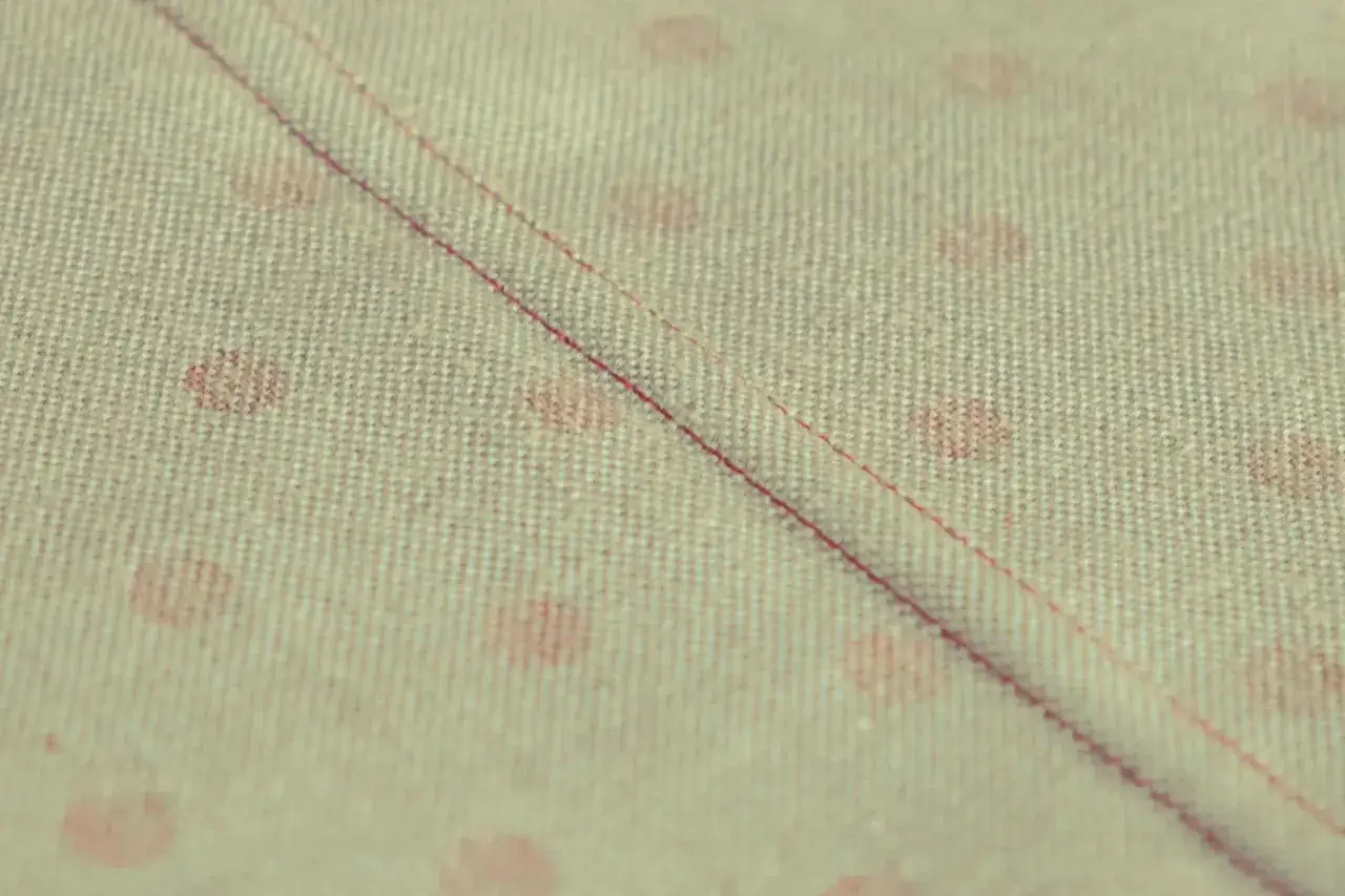 Primo piano di tessuto con pois rosa e due tipi di cuciture rosse parallele.