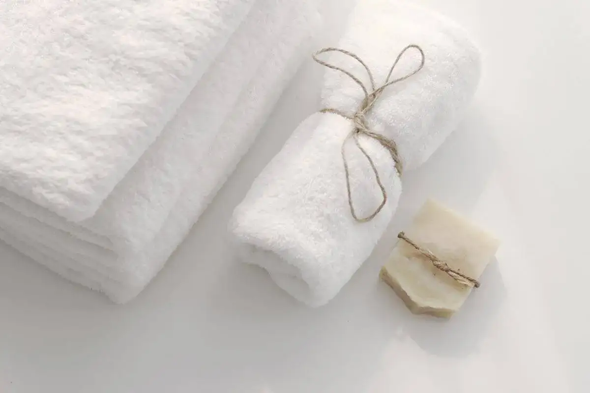 Asciugamani bianchi piegati e arrotolati con spago, come in un b&b. Un sapone artigianale completa la scena.