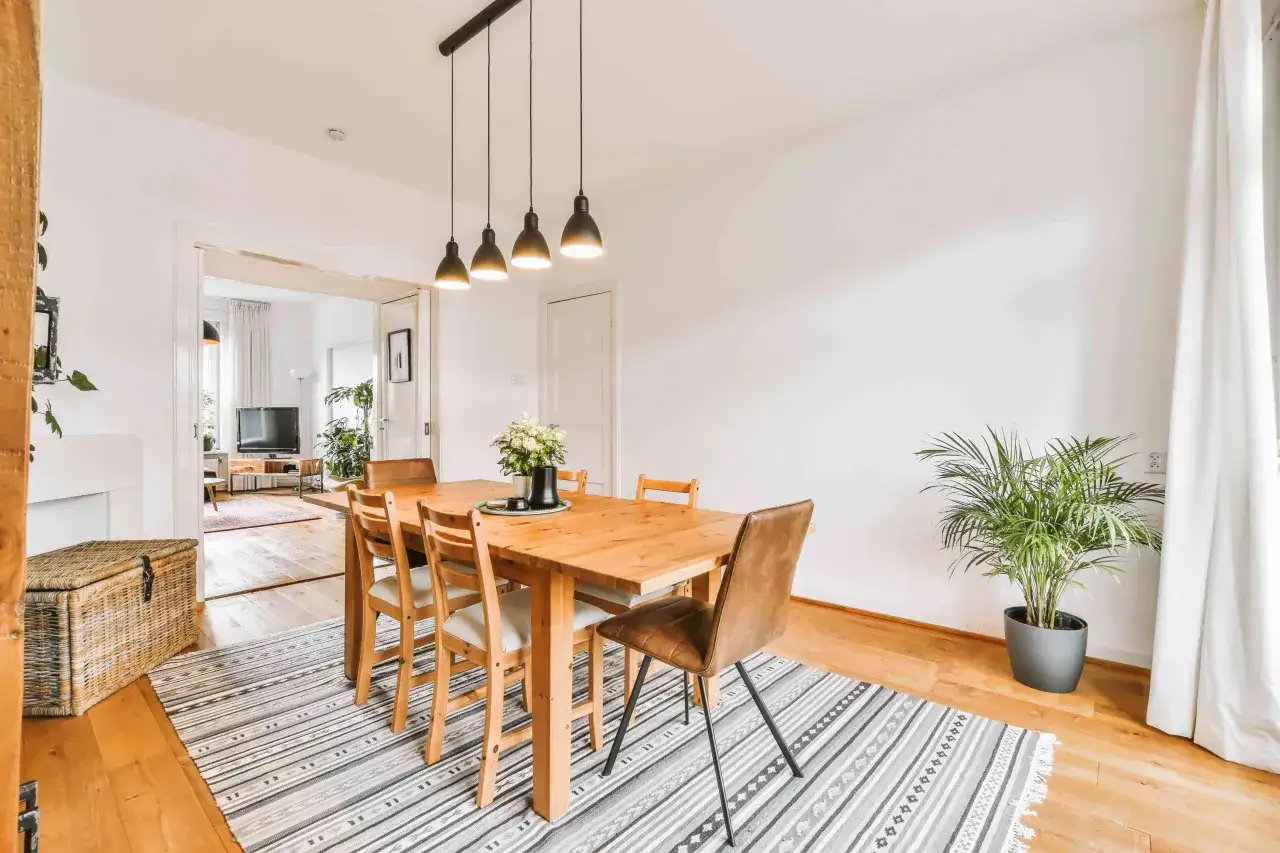 Un tappeto sotto il tavolo da pranzo aggiunge calore e stile. Questo spazio moderno presenta un tavolo in legno con sedie, illuminato da lampade a sospensione.