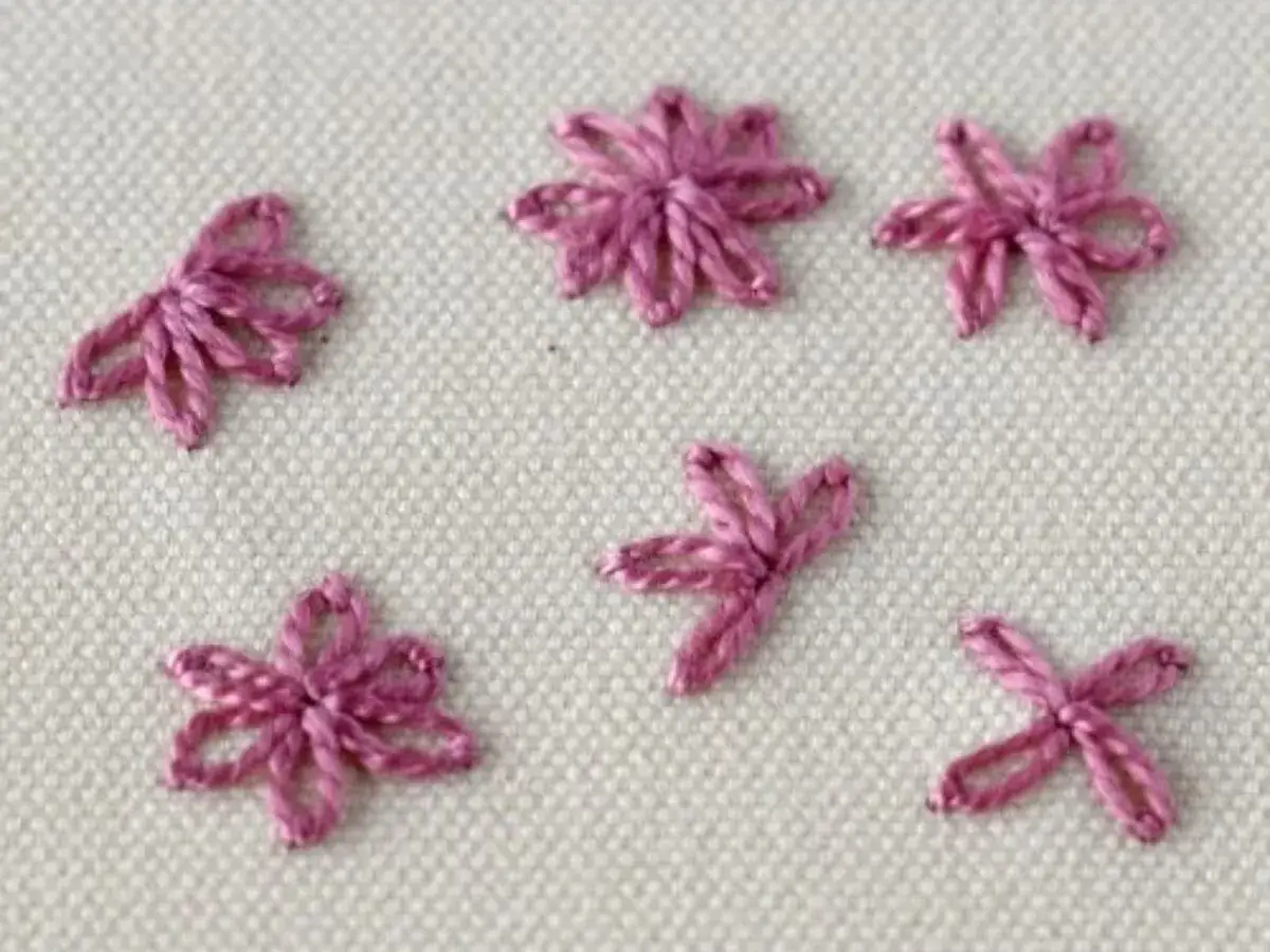 Ricamo di piccole margherite rosa su tessuto grezzo.