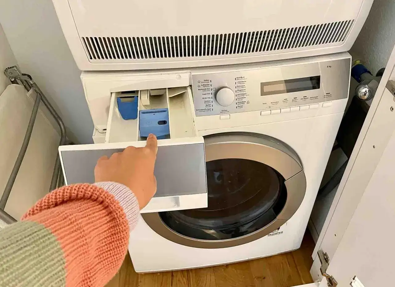 Mano che indica il cassetto del detersivo della lavatrice, dove si mette l'ammorbidente per ammorbidire il bucato.