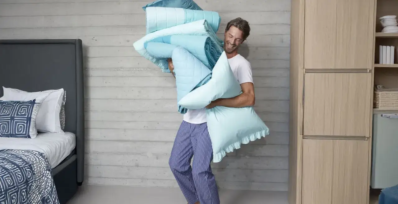 Uomo sorridente con un mucchio di lenzuola azzurre, pronto a sistemare tutto nell'armadio.