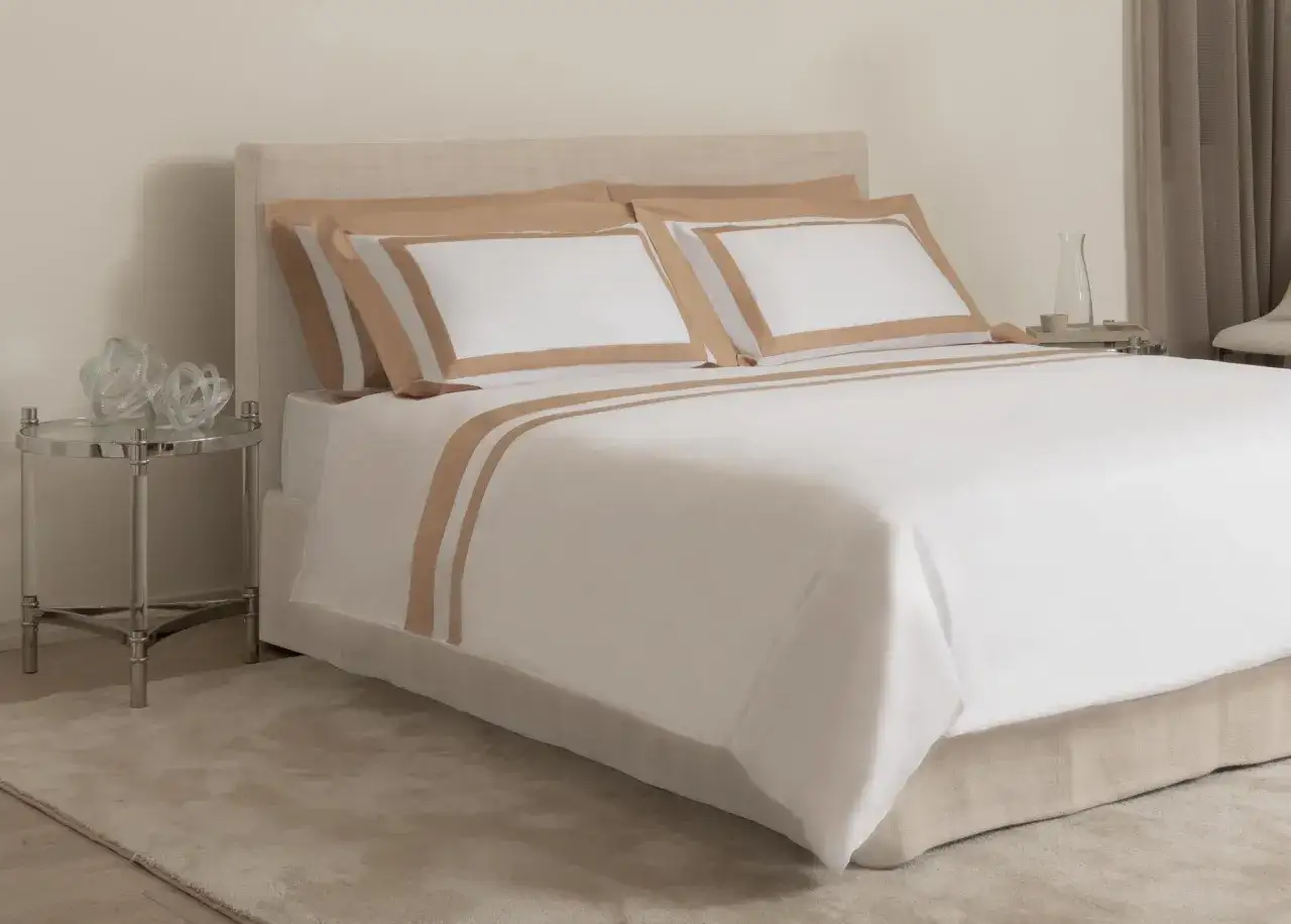 Letto con copripiumino bianco e bordi color sabbia. Due cuscini coordinati.