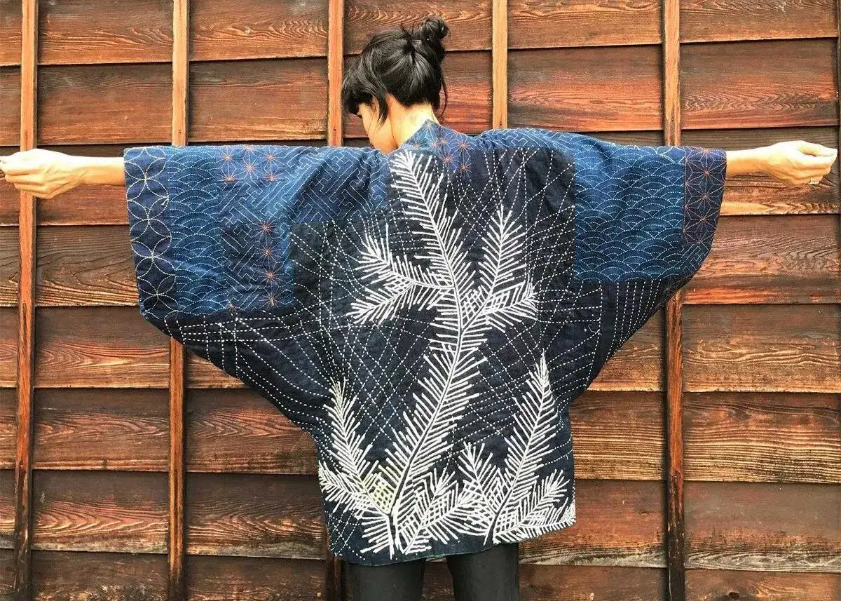 Giacca blu con ricami bianchi a forma di foglie e motivi geometrici, ispirata ai tradizionali sashiko schemi.