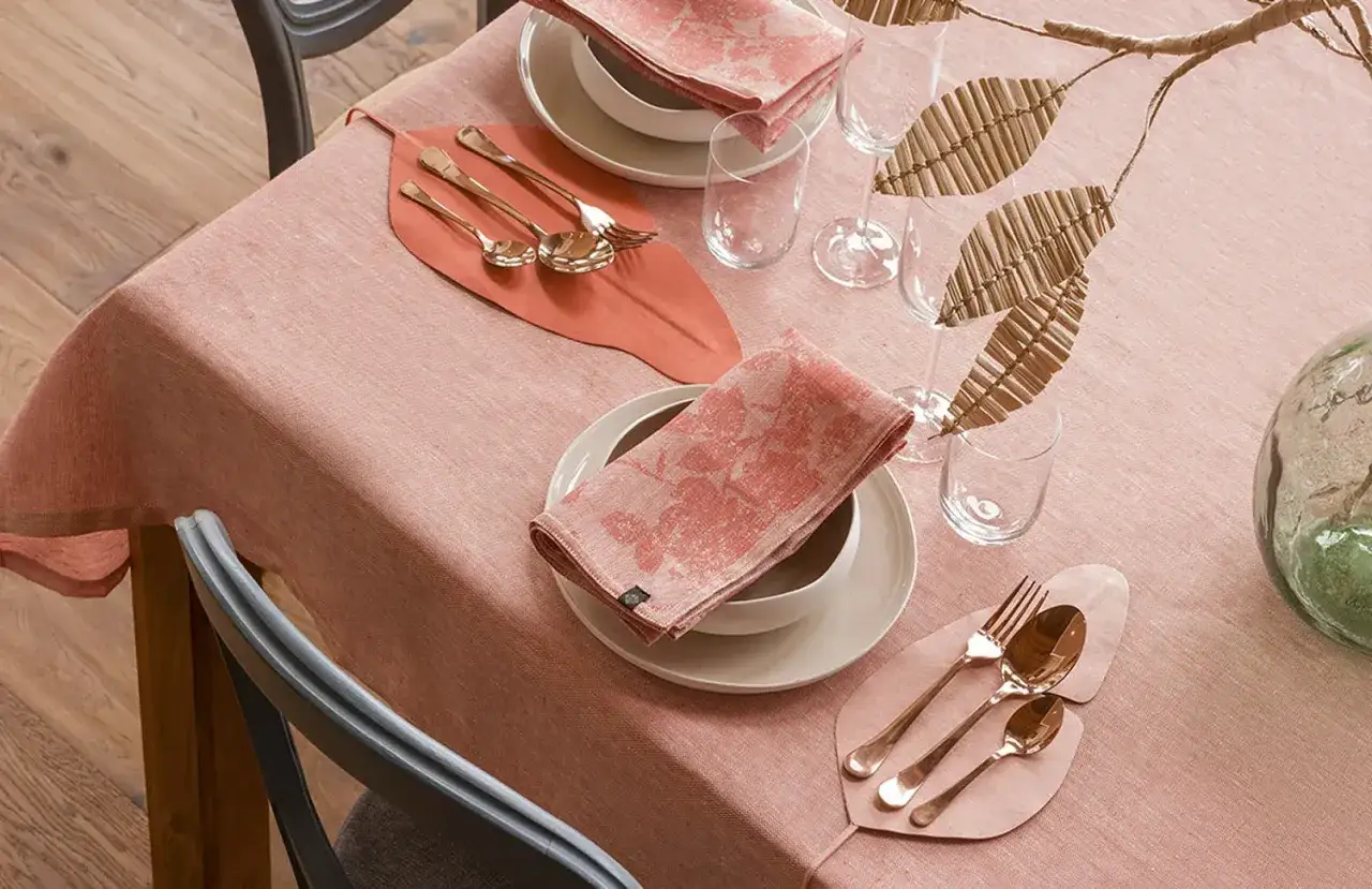 Tavola apparecchiata con tovaglia rosa, piatti, posate dorate e tovaglioli coordinati. Un'idea su come abbinare i piatti alla tovaglia per un'elegante mise en place.