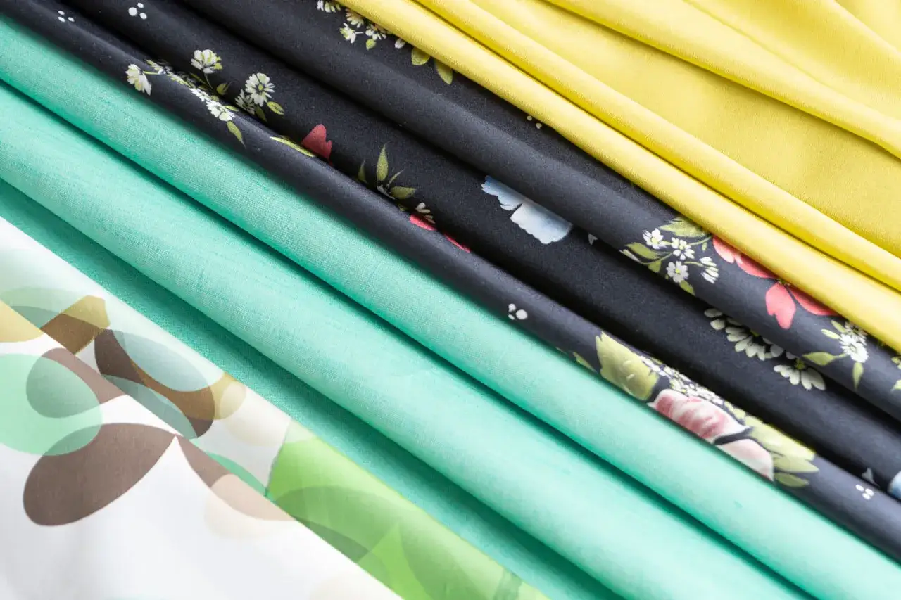 Tessuti colorati, tra cui uno a fiori e uno giallo, perfetti per imparare come cucire un vestito estivo semplice.