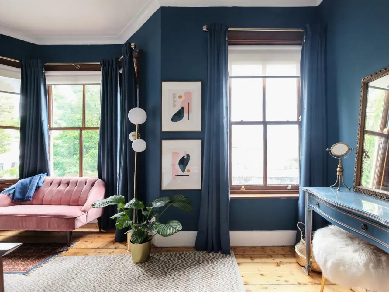 Elegante abbinamento colori tende pareti blu scuro con divano rosa cipria e tocchi dorati.